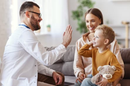 kid and her mother visiting their doctor. kid give high five to his doctor
